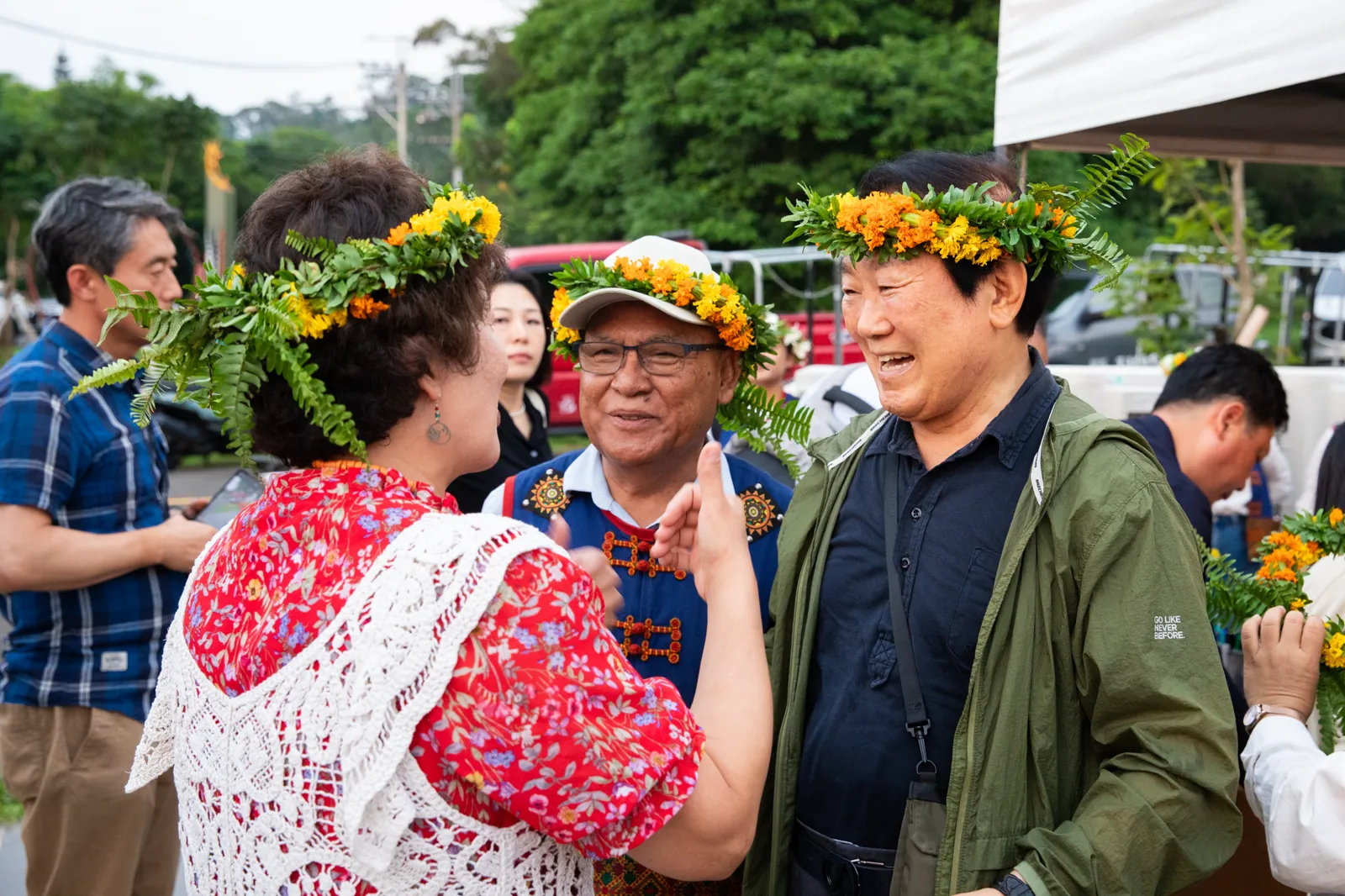 三位頭戴花環的與會來賓在活動現場相談致意